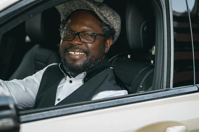 Herr Doglo sitzt lächelnd auf dem Fahrersitz eines Taxis während einer Krankenfahrt in Bremen.